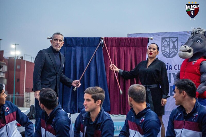 Jugadores del Atlante F.C. posan junto a la mascota del equipo, un burro, y directivos en la develación de una placa.