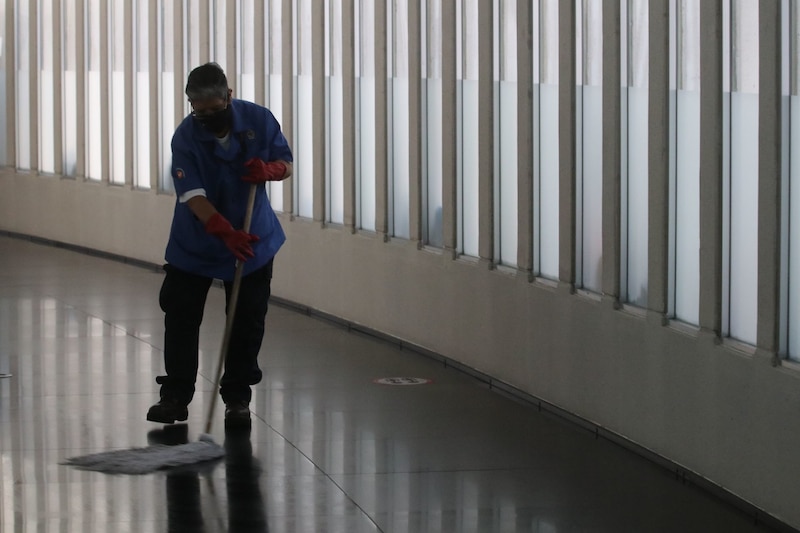 Un hombre con uniforme azul y guantes rojos limpia el suelo con una mopa.