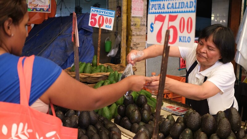 Title: Mujer comprando aguacates en un mercado