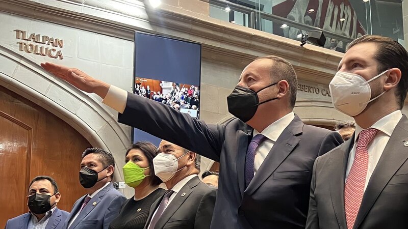Un político pronuncia un discurso ante un grupo de personas en un recinto cerrado.