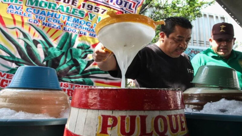 Un hombre vierte pulque de un recipiente a otro