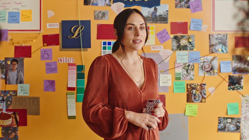 Mujer mirando su teléfono con una pared de fotos detrás