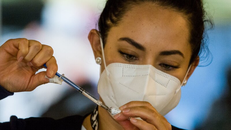 Mujer con mascarilla sosteniendo una jeringa con una aguja