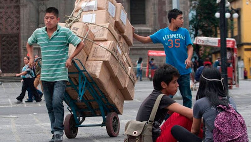 Un hombre empuja una carreta cargada de cajas por una calle de la ciudad.