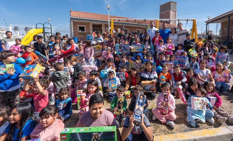 Grupo de niñas y niños sonrientes sosteniendo juguetes en un evento comunitario de Día de Reyes