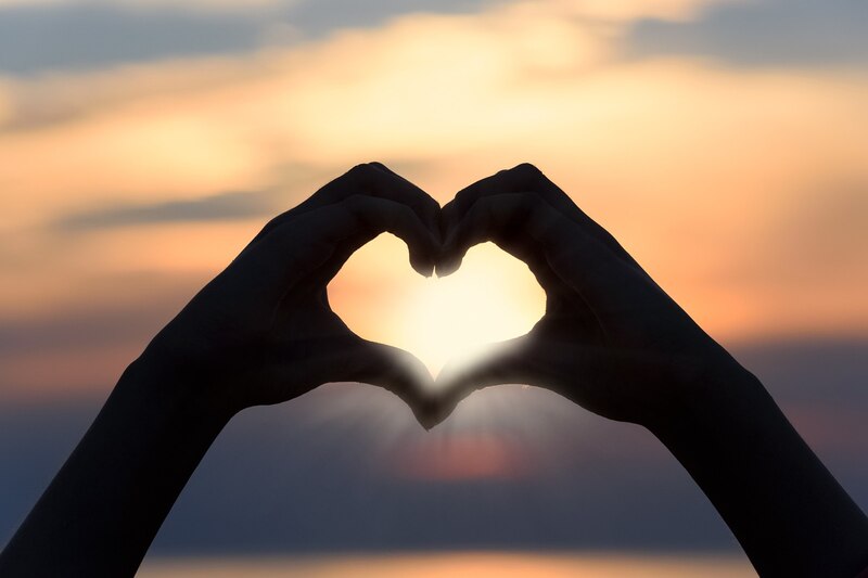 Manos formando un corazón con el atardecer de fondo