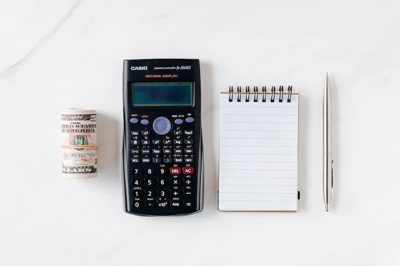 Calculadora Casio, dinero en efectivo y libreta de notas sobre fondo blanco