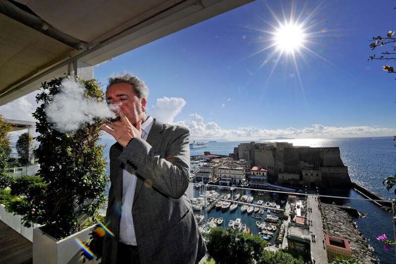 Un hombre fumando en una terraza con vistas al mar