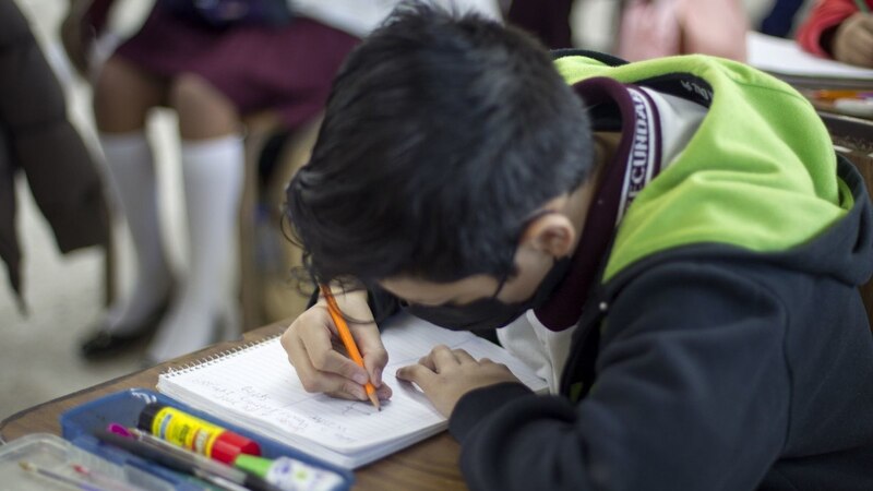 Niño con cubrebocas escribiendo en su cuaderno
