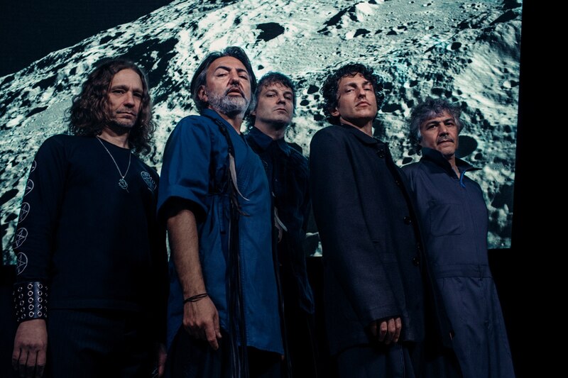 Cuatro hombres vestidos con ropa casual posan para una foto con la luna de fondo