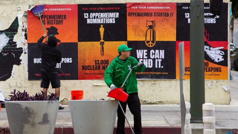 Un hombre barre la acera junto a un cartel que dice "Podemos acabar con las armas nucleares".