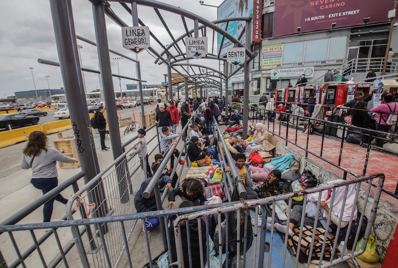 Un grupo de personas espera en la frontera entre México y Estados Unidos.