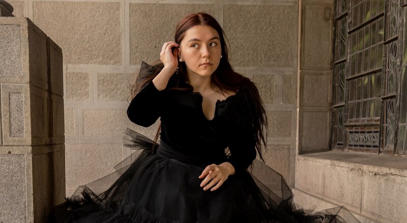 Elegante mujer joven con vestido negro sentada en las escaleras