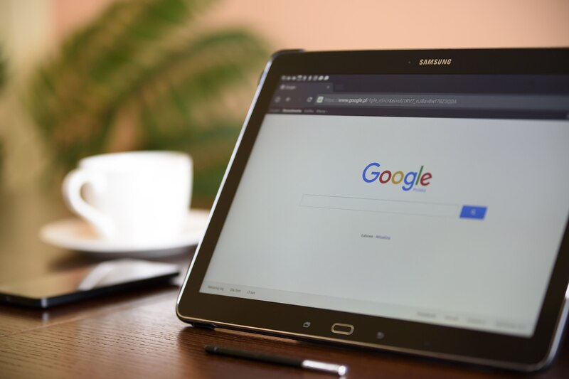 Una taza de café sobre una mesa, junto a una tablet que muestra el buscador de Google.