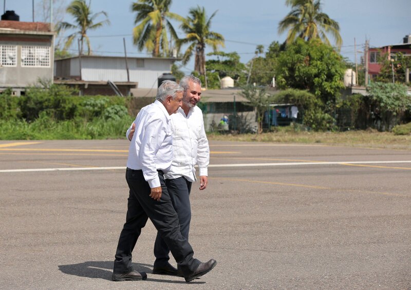 Dos hombres caminan juntos por una calle en un pueblo latinoamericano.