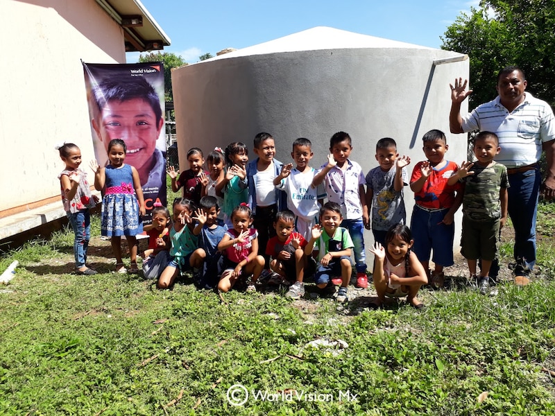 Niños sonríen frente a un tanque de agua en una comunidad rural