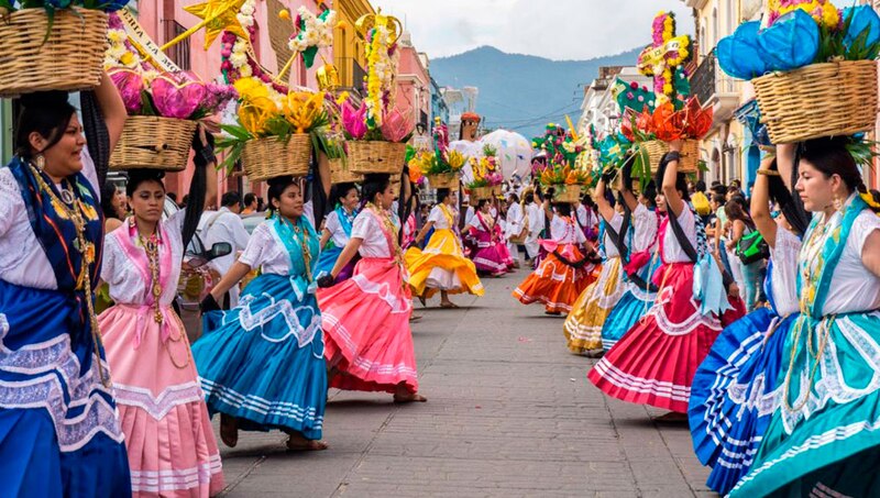 Mujeres indígenas en traje tradicional mexicano bailando en una calle durante una celebración.