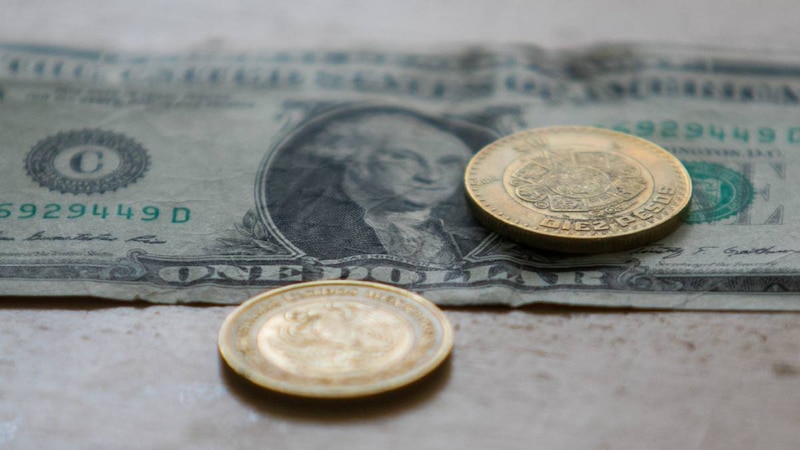 Monedas mexicanas sobre un billete de dólar estadounidense