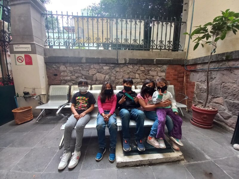 Cuatro niños sentados en una banca en el exterior con cubrebocas