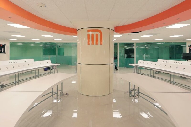 Oficinas modernas con escritorios y sillas blancas, separadas por mamparas de cristal.