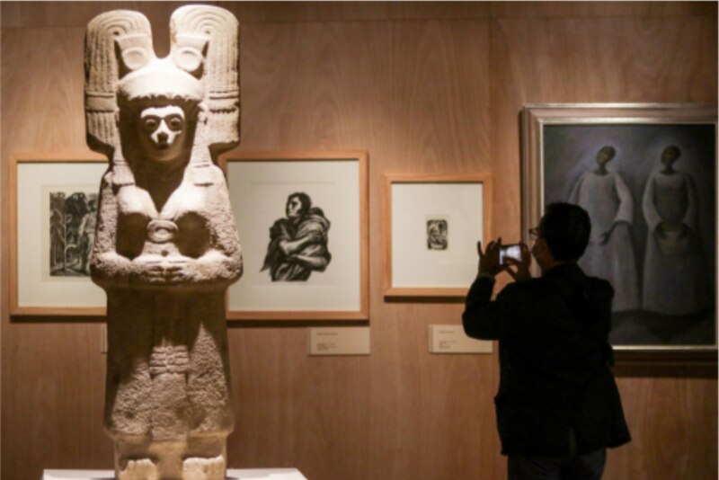 Visitante tomando una foto de una escultura prehispánica en un museo