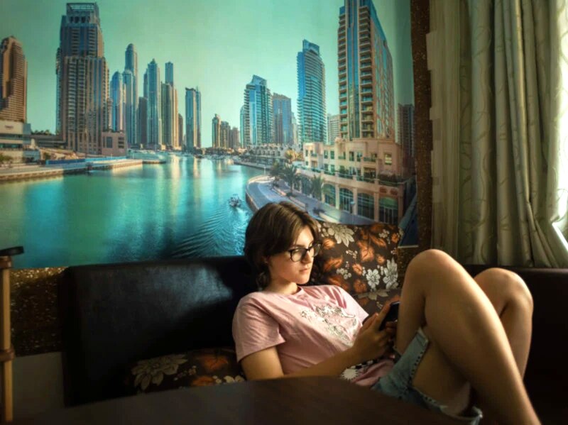 Joven mirando su teléfono en una habitación con un mural de una ciudad