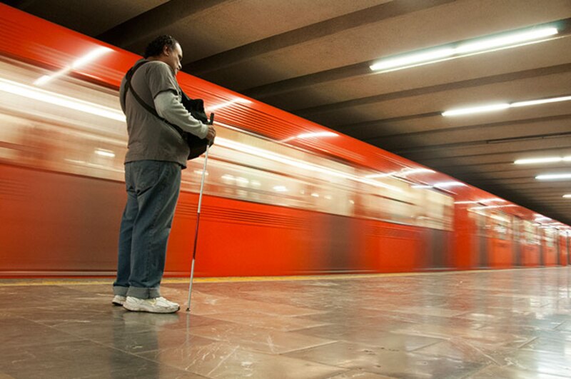 Un hombre invidente espera el metro en la estación.