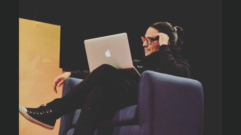 Un hombre joven sentado en un sillón mira su laptop.