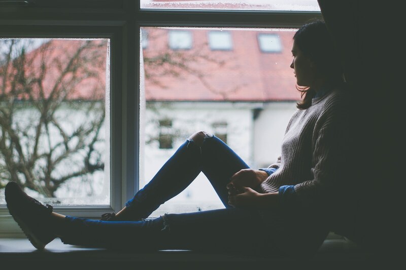 Mujer sentada en el alféizar de una ventana mirando hacia afuera