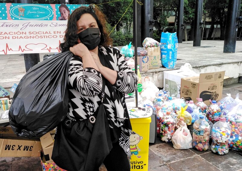 Una mujer sostiene una bolsa negra llena de botellas de plástico reciclado.