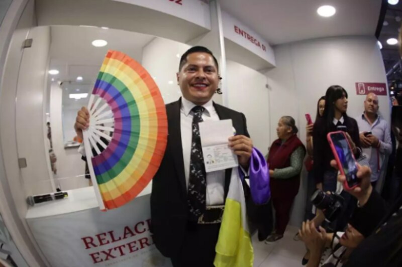 Un hombre sostiene un pasaporte y una bandera arcoíris