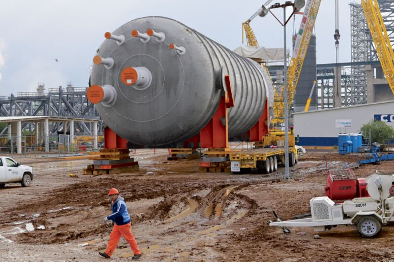 Un trabajador camina junto a un gran recipiente industrial.