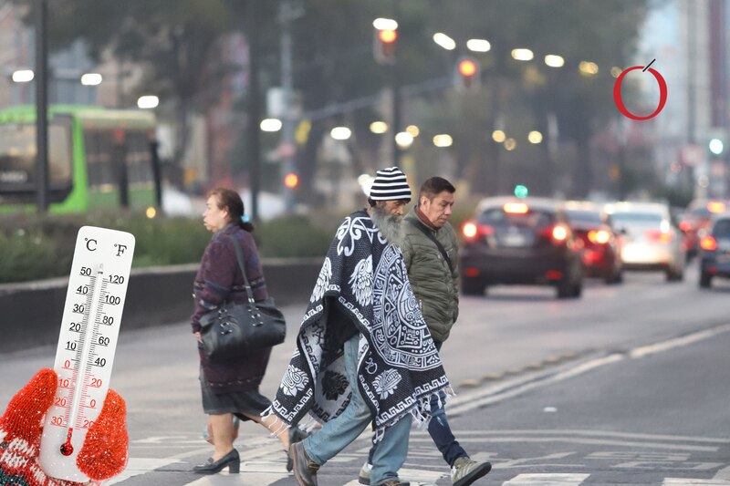 Una persona se protege del frío con un gabán mientras camina por la calle