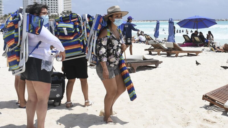 Mujeres con cubrebocas cargando sillas de playa en Cancún