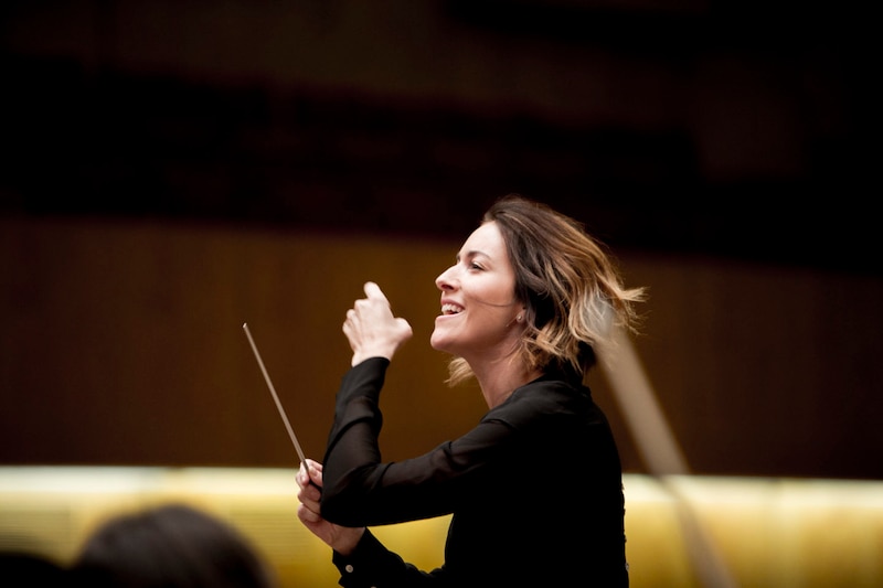 La directora de orquesta Marin Alsop sonríe mientras dirige una orquesta.