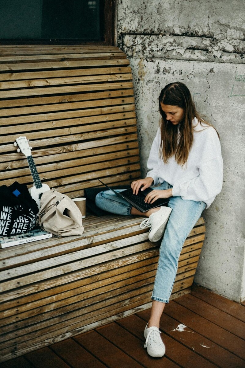 Mujer joven sentada en un banco usando su laptop