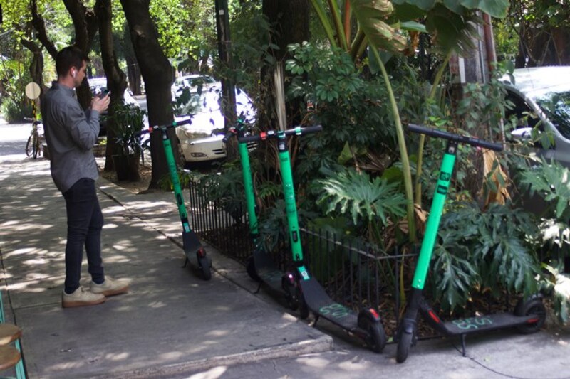 Hombre mirando su teléfono junto a una fila de scooters eléctricos verdes