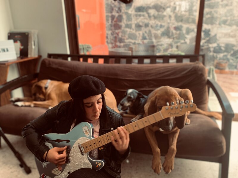 Mujer tocando la guitarra en el sofá con dos perros a su lado