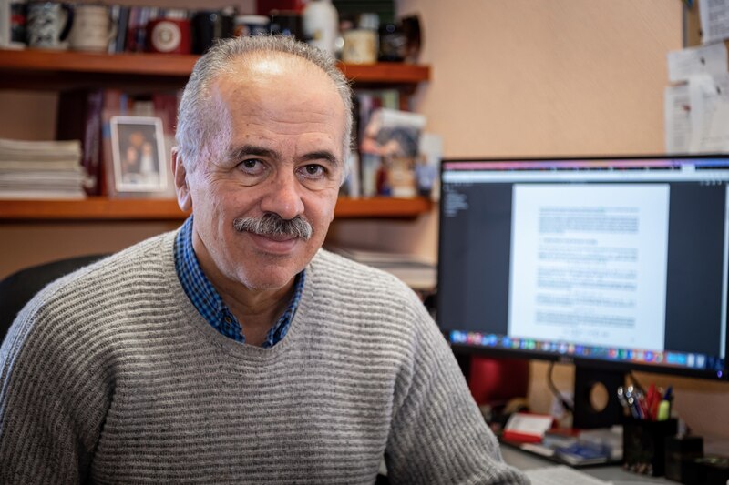 Un hombre mayor con bigote y pelo blanco sonríe a la cámara.