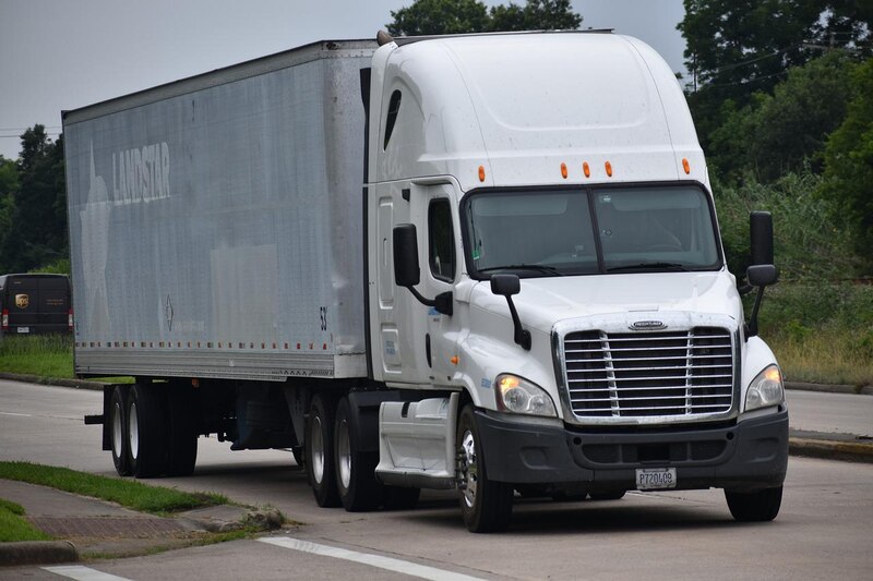 Un camión blanco de carga pesada Freightliner Cascadia de la empresa Landstar System, Inc. circula por una carretera.