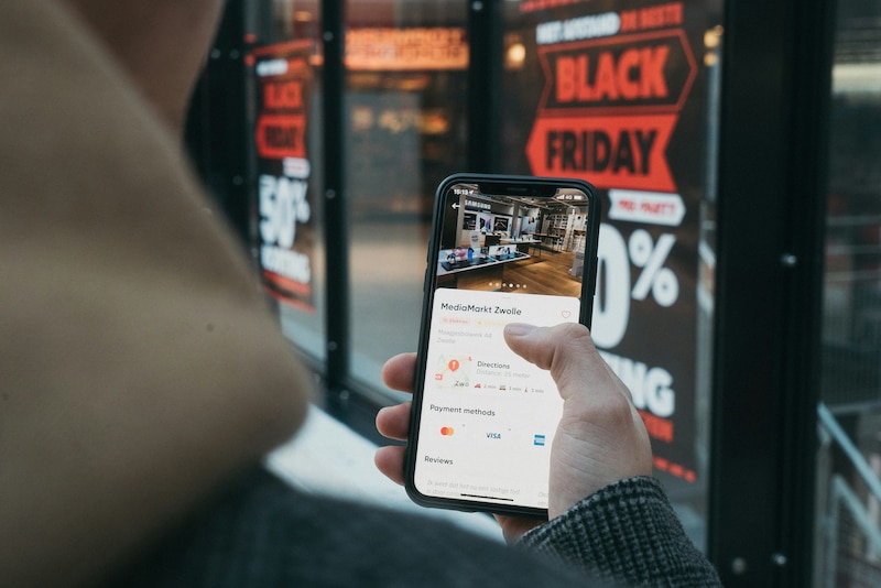 Persona sosteniendo un celular frente a una tienda con ofertas del Black Friday.