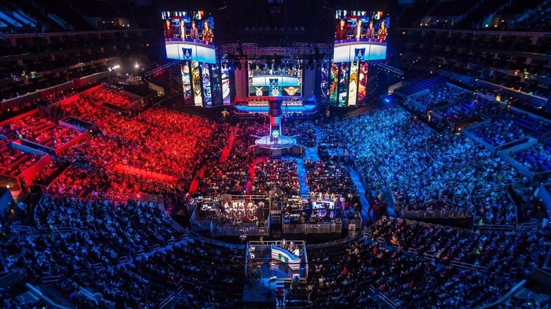 La imagen muestra a un grupo de personas en un estadio viendo un torneo de videojuegos.