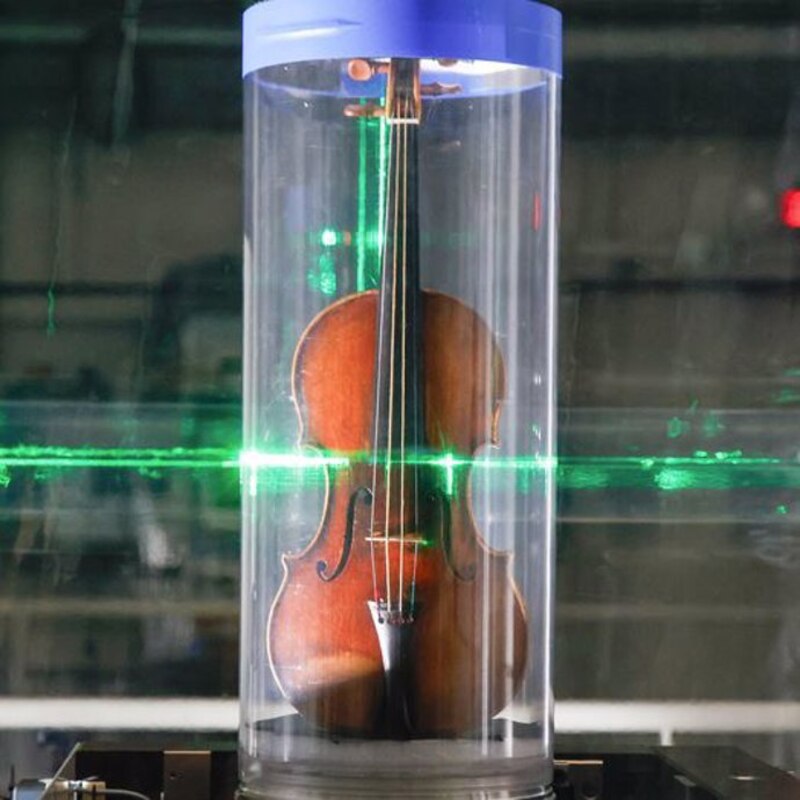 Un violín dentro de un cilindro de vidrio con un láser verde que lo atraviesa
