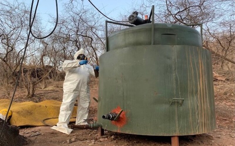 Un trabajador con traje de protección inspecciona un tanque de almacenamiento de líquidos.
