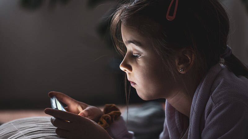 Niña usando un teléfono móvil en la cama