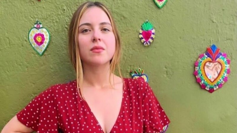 Jovencita en vestido rojo de lunares blancos, parada frente a un muro verde decorado con corazones de colores.