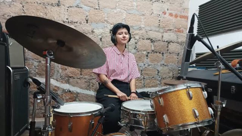 Baterista mujer tocando la batería en un estudio de grabación.