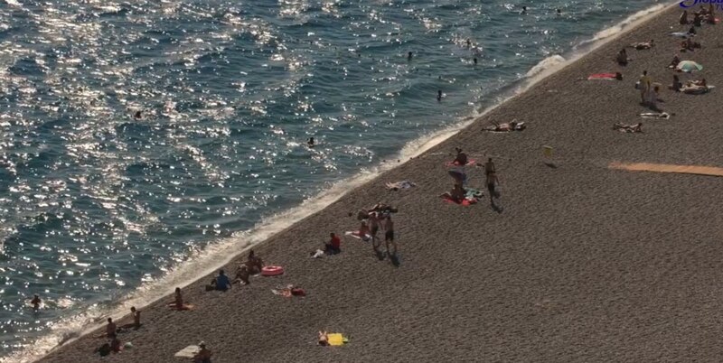 Playa de arena con gente tomando el sol y bañándose en el mar