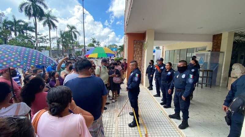 Policías vigilan una fila de personas que esperan para entrar a un edificio.