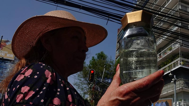Mujer sosteniendo una botella de vidrio transparente con un líquido transparente en su interior